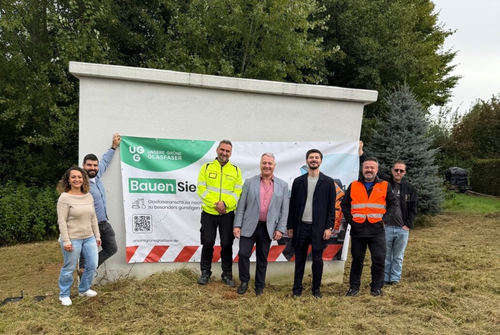 Gruppenfoto bei der Vorstellung eines Glasfaserprojekts von Unsere Grüne Glasfaser mit beteiligten Personen und Banner.